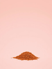 A minimalistic mound of brown granules on a soft pink background.