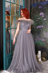 Fototapeta premium Beautiful girl with red hair in a long gray dress