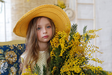 Girl in a hat with a bouquet of yellow flowers in her hands in a photo studio