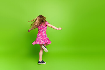 Happy young girl spinning in a pink dress on a vibrant green background, expressing joy and energy...