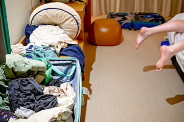 open suitcase and messy clothes in hotel room, authentic travel with children and teenagers