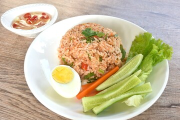 spicy fried rice with mashed salmon topping half boiled egg eat couple fresh vegetable on plate dressing slice chili and garlic fish sauce 
