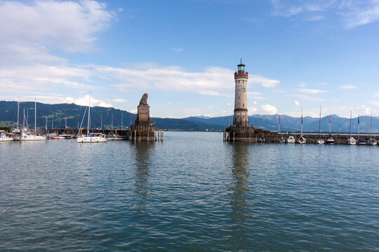 A wide-angle view of the iconic harbor entrance of Lindau on Lake Constance (Bodensee), under a bright blue sky with scattered clouds