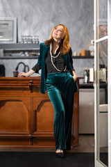 Elegant mature woman in teal velvet suit sitting at bar counter with cup of coffee in hand surrounded by black and white art photography