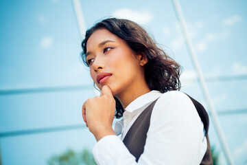 Confident young businesswoman reflecting on success outdoors on a sunny day with an urban modern...