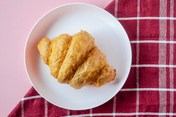 Freshly baked croissant on plate, top view. Flat lay. French pastry closeup photo. Buttered bread croissant. 