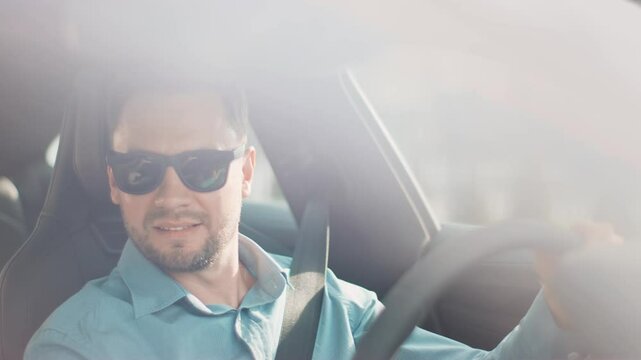 Handsome Caucasian male wearing sunglasses driving car during bright sunny day. Resting hand on head and looking out with slight smirk. Enjoying solo ride while soaking in daylight views.