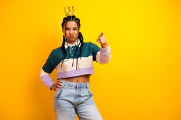 Confident young woman with braids wearing a stylish casual top, pointing assertively against a...