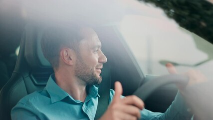 Happy Caucasian male gripping steering wheel with both hands while smiling and mouthing lyrics. Singing song during relaxing solo drive. Enjoying music and bright mood inside moving car. - Powered by Adobe
