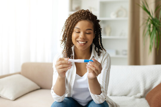 Happy black woman looking at positive pregnancy test at home. Excited expression showing joy and surprise during emotional moment of discovering pregnancy, closeup