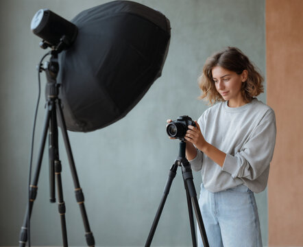 Young female photographer adjusting camera settings in professional studio