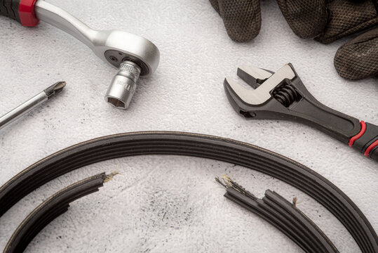 A broken drive belt from a car's generator and a number of tools, such as a screwdriver, adjustable wrench, and a socket wrench, laid out on a table.