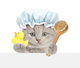 Funny tiny kitten with shower cap on it head looks above blank white banner holds shower brush and...
