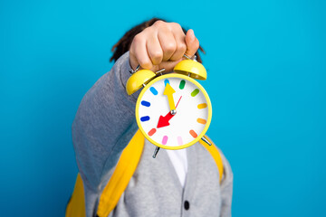 Cheerful schoolboy holding a bright yellow clock against a blue background, emphasizing time...