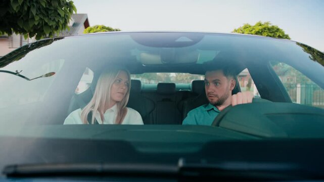 Serious blonde woman frowning and turning head toward driver with confused look. Bearded man glaring back while gripping wheel. Tension rising. Sitting in uncomfortable silence during small stop.