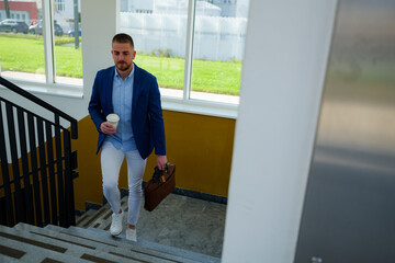 Young manager walking downstairs at the end of the workday, holding a coffee cup and briefcase, heading home or to a meeting with colleagues