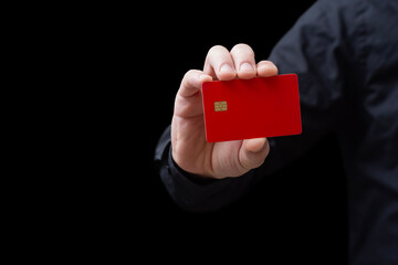 Close-up of a hand holding a red credit or debit card with chip on a black background. Concept of...