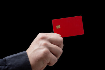 Close-up of a hand holding a red credit or debit card with chip on a black background. Concept of banking, finance, contactless payment and online shopping.