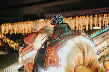A young woman dressed for winter enjoys a brightly lit carnival ride surrounded by festive...