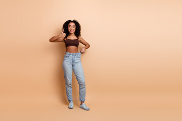 Beautiful young woman with afro curls smiling and giving thumbs up on beige background, casual...