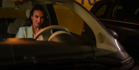 Young businesswoman driving her car through an underground parking lot after a long day at work, confidently gripping the steering wheel and focused on the road ahead