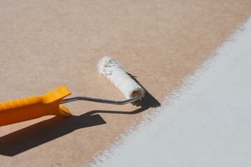 Close-up a paint roller with a yellow handle applying a smooth layer of white paint onto a brown surface. Concept home renovation and DIY projects.