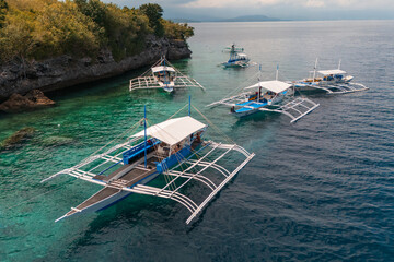 Moored Outrigger Bangka Boats Against a Dramatic Limestone Shoreline in sunny paradise Pescador...