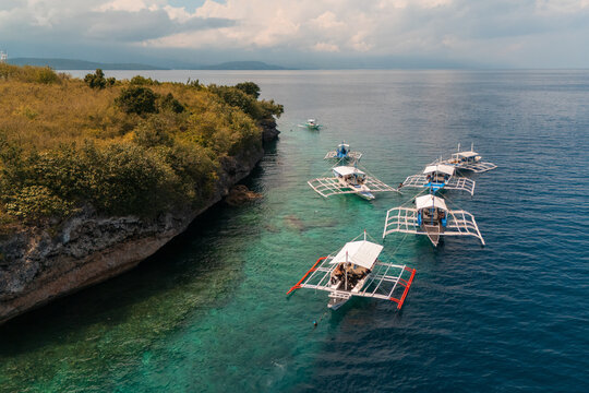 Moored Outrigger Bangka Boats Against a Dramatic Limestone Shoreline in sunny paradise Pescador Island  &ndash; Moalboal, Cebu, Philippines