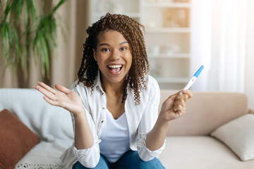 Black woman excitedly reacting to positive pregnancy test, holding it up with wide smile. Powerful...