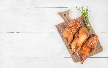 Three whole smoked quails are beautifully arranged on a rustic wooden cutting board with fresh...