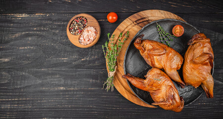 Three perfectly smoked quails are artfully arranged on a dark rustic plate with fresh thyme, coarse...