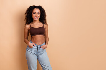 Young woman with curly hair wearing a stylish outfit smiling confidently against a beige background...