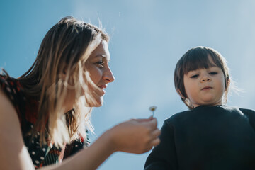 A caring woman interacts with a child, highlighting tenderness and connection outdoors in natural...