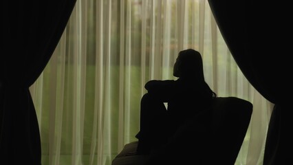Silhouette of a distressed woman in front of backlit curtains