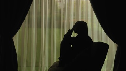 Silhouette of a distressed woman in front of backlit curtains