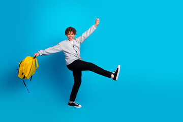 Excited young schoolboy with a cheerful expression holding a bright yellow backpack against a...