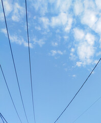 Fototapeta premium Power lines converge against a bright blue sky scattered with fluffy white clouds.