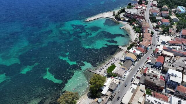hovering above Benitses coastline with turquoise water, panning left along coastal road with Benitses Beach, Paralia Mpenitses beach, parking slots and Marian in background - 4k aerial video footage