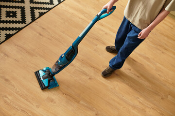 Young man tidying up his home with a vacuum cleaner on a sunny afternoon