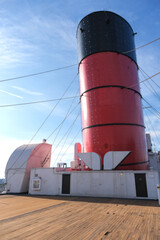 Red and black funnel of historic oceanliner ocean liner Mary against deep blue sky with clouds	