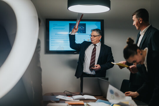 Corporate team engaged in a brainstorming session in a modern office environment, emphasizing collaboration, leadership, and analysis of key business data displayed on a screen.