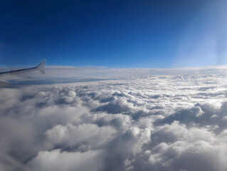 Plane flying over clouds, view from airplane window, fluffy cloudscape and blue sky