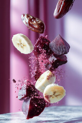 Beetroot, banana and dates floating with water droplets on pink background