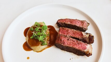 close up of three pieces of medium rare grilled beef steak and mashed potato with sauce on the side, and copy space
