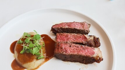 close up of three pieces of medium rare grilled beef steak and mashed potato with sauce on the...