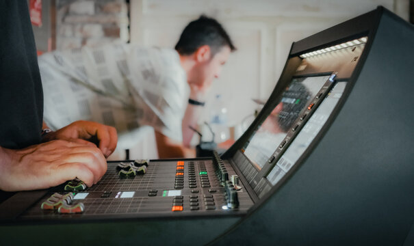 Two audiovisual engineers working together on a live event in a room. In the foreground, one of them's hands working on the audio mixer.