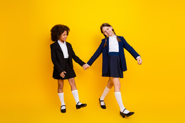 Fototapeta premium Happy schoolgirls holding hands on vibrant yellow background showcasing friendship and diversity in stylish school uniforms