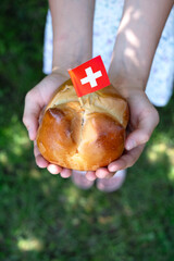 Swiss national August bread bun with a swiss flag in child hands.