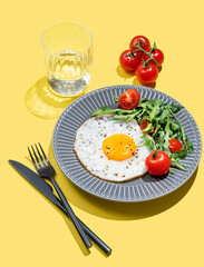Fried eggs with arugula and cherry tomatoes on a dark plate on a yellow background