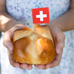 Swiss traditional August bread bun with a swiss flag in child hands, square format.
